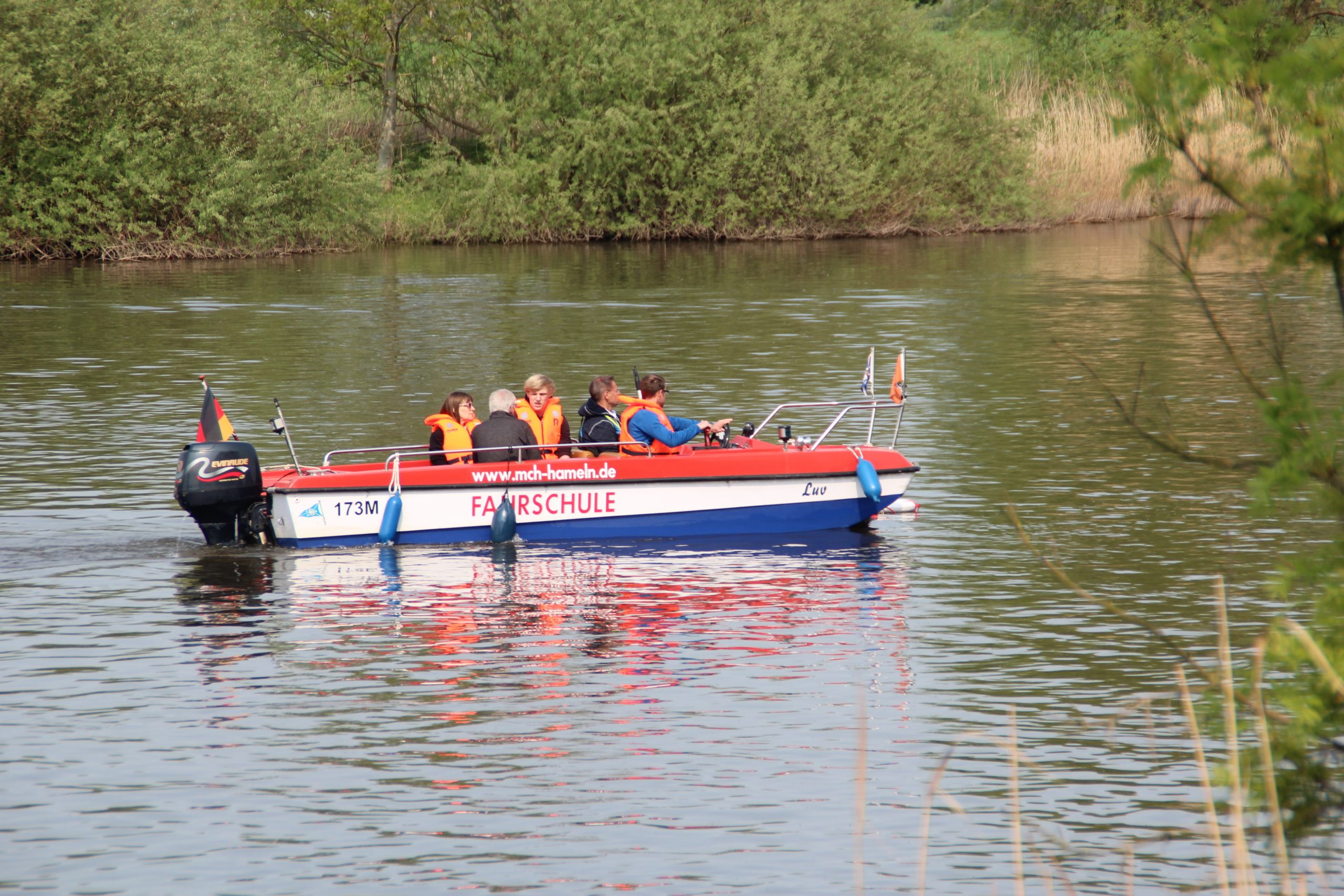 Ein rot-weiß-blaues Boot fährt auf dem Wasser; die Insassen tragen orangene Rettungswesten.